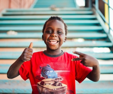 Young boy smiling with hands up in the form of a peace sign.